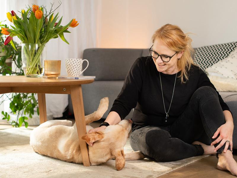 Frau streichelt Hund in Wohnung